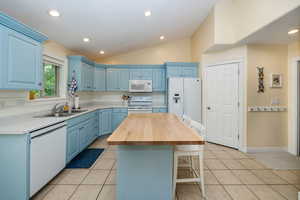 Kitchen with vaulted ceiling, white appliances, blue cabinets, a center island, and sink