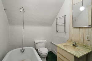 Bathroom featuring a tub to relax in, vanity, toilet, and lofted ceiling