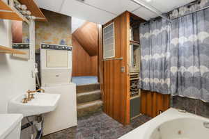 Bathroom featuring stacked washer and clothes dryer, toilet, a bathtub, and a drop ceiling