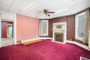 Living room with a drop ceiling, a brick fireplace, ceiling fan, and carpet