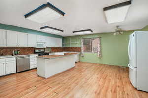 Large kitchen featuring a kitchen island, white appliances, light hardwood / wood-style floors, ceiling fan, and white cabinets