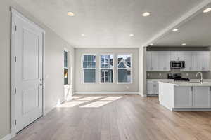 Kitchen featuring white cabinets, backsplash, light hardwood / wood-style flooring, appliances with stainless steel finishes, and a textured ceiling