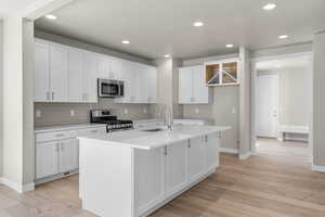 Kitchen featuring a center island with sink, stainless steel appliances, sink, and white cabinetry