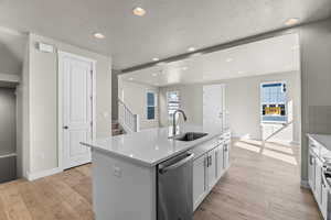 Kitchen featuring a textured ceiling, an island with sink, sink, appliances with stainless steel finishes, and light hardwood / wood-style floors