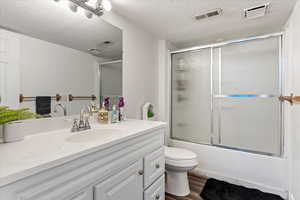 Full bathroom featuring a textured ceiling, vanity, bath / shower combo with glass door, toilet, and hardwood / wood-style flooring