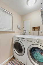 Clothes washing area with light tile patterned floors, washing machine and clothes dryer, and a textured ceiling