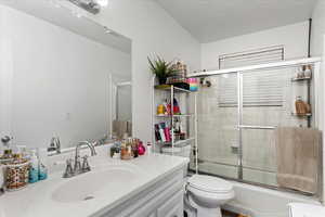 Full bathroom featuring toilet, bath / shower combo with glass door, a textured ceiling, and vanity