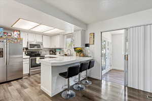 Kitchen with light hardwood / wood-style flooring, appliances with stainless steel finishes, kitchen peninsula, sink, and white cabinets