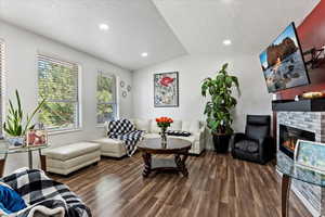 Living room with lofted ceiling, dark hardwood / wood-style floors, a brick fireplace, and a textured ceiling