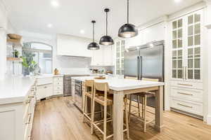 Kitchen with built in fridge, crown molding, a center island, light wood-type flooring, and white cabinets