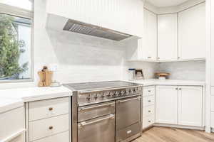 Kitchen featuring light hardwood / wood-style flooring, tasteful backsplash, white cabinetry, custom exhaust hood, and high end range