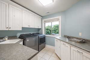 Laundry room with a textured ceiling, cabinets, light tile patterned floors, independent washer and dryer, and sink