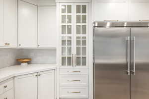 Kitchen featuring backsplash, built in refrigerator, light stone counters, and white cabinetry