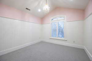 Carpeted empty room with vaulted ceiling and a chandelier