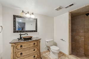 Bathroom with tiled shower, vanity, toilet, and a textured ceiling