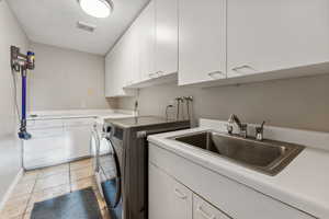 Washroom featuring washing machine and clothes dryer, cabinets, and sink