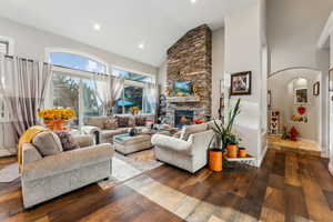 Living room featuring dark wood-type flooring, high vaulted ceiling, and a stone fireplace