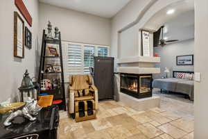 Master suit sitting area featuring a multi sided fireplace and ceiling fan