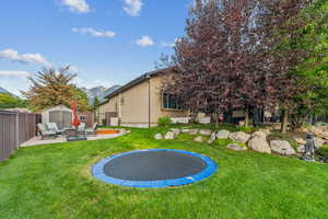 View of yard with a trampoline, a shed, and a patio area with fire pit