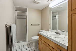 Bathroom featuring a shower with door, tile patterned floors, toilet, vanity, and a textured ceiling