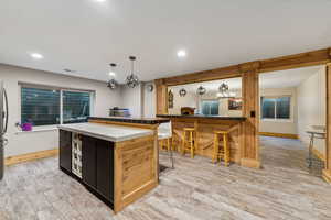 Kitchen with light wood-type flooring, pendant lighting, stainless steel fridge, a kitchen breakfast bar, and a center island