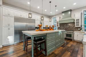 Kitchen featuring high end appliances, dark hardwood / wood-style flooring, a center island, custom range hood, and white cabinets