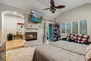 Primary Bedroom with a tiled fireplace, vaulted ceiling, access to exterior, and ceiling fan