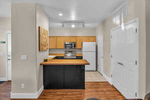 Kitchen featuring stainless steel appliances, light brown cabinets, butcher block countertops, and light hardwood / wood-style floors