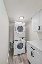 Laundry area with hardwood / wood-style floors, cabinets, and stacked washer / dryer