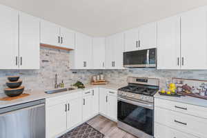 Kitchen with light hardwood / wood-style flooring, stainless steel appliances, sink, decorative backsplash, and white cabinets