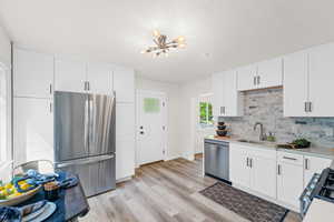 Kitchen featuring a notable chandelier, white cabinetry, light hardwood / wood-style flooring, sink, and appliances with stainless steel finishes