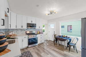 Kitchen with light hardwood / wood-style flooring, a notable chandelier, backsplash, stainless steel appliances, and white cabinetry