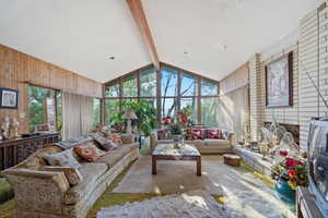 Carpeted living room with a textured ceiling, a healthy amount of sunlight, wood walls, and beam ceiling