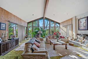 Living room with beamed ceiling, wooden walls, and light carpet