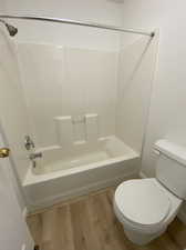 Bathroom with toilet, hardwood / wood-style floors, and bathtub / shower combination