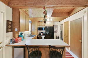 Kitchen featuring beam ceiling, a kitchen bar, kitchen peninsula, sink, and stainless steel appliances