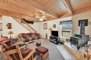 Tiled living room featuring wooden ceiling, ceiling fan, a wood stove, and beam ceiling