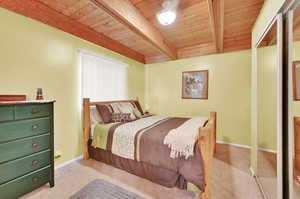 Bedroom with wooden ceiling, beamed ceiling, light colored carpet, and a closet