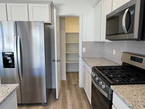 Kitchen with backsplash, light stone counters, stainless steel appliances, and white cabinetry