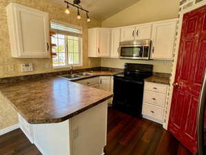 Kitchen featuring lofted ceiling, black / electric stove, kitchen peninsula, and white cabinetry