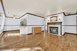 Unfurnished living room with light hardwood / wood-style flooring, ceiling fan, ornamental molding, and a tile fireplace