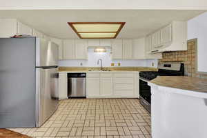 Kitchen with backsplash, stainless steel appliances, white cabinetry, sink, and premium range hood