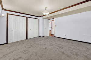 Unfurnished bedroom featuring carpet flooring, ornamental molding, and multiple closets