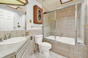 Full bathroom with shower / bath combination with glass door, vanity, tile walls, toilet, and tile patterned floors