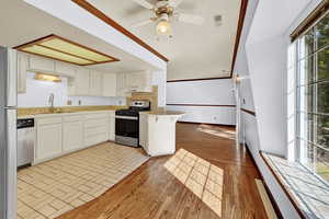 Kitchen featuring appliances with stainless steel finishes, ornamental molding, white cabinetry, ceiling fan, and light wood-type flooring