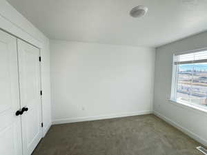 Unfurnished bedroom with dark carpet, a textured ceiling, and a closet