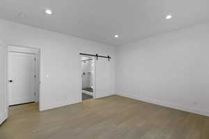 Unfurnished bedroom with a barn door, ensuite bathroom, and light hardwood / wood-style floors