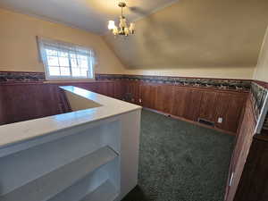 Interior space with lofted ceiling, dark carpet, a chandelier, and wood walls