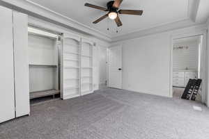 Unfurnished bedroom featuring ceiling fan, carpet floors, and a tray ceiling