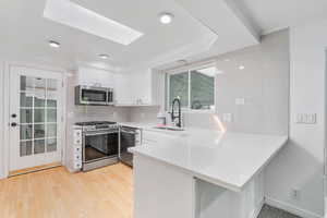 Kitchen featuring white cabinets, appliances with stainless steel finishes, kitchen peninsula, and light hardwood / wood-style flooring